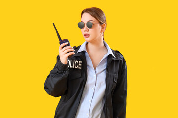 Female police officer with radio transmitter on yellow background