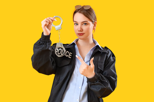Female police officer pointing at handcuffs on yellow background - Powered by Adobe