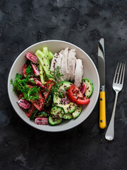 Delicious diet lunch - boiled chicken and fresh vegetable salad with seasonal vegetables on a dark background, top view