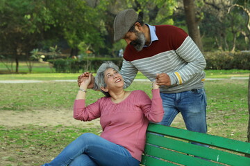 Mid aged couple sitting on the bench in a lush green serene environment having a good time together. They are happily enjoying their time. smiles all around.