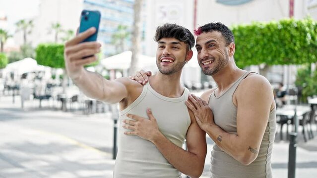 Two men couple smiling confident having video call at coffee shop terrace