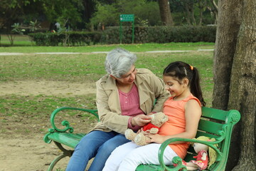 Happy Indian Grand parents with grand daughter in a lush green serene park. They are playing on park bench.