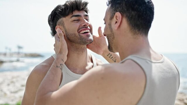 Two men couple smiling confident hugging each other and kissing at seaside