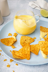 Plate with pitcher of tasty cheddar cheese sauce and nachos on white grunge background