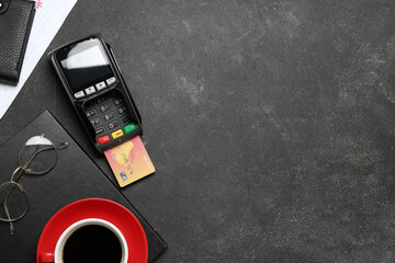 Credit card with payment terminal and cup of coffee on black table