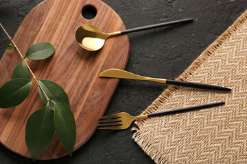 Board with golden cutlery on black background