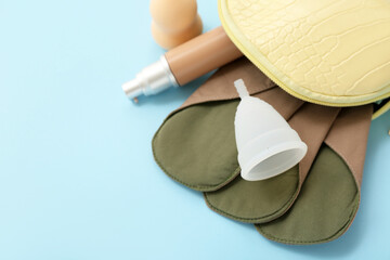 Lady's cosmetic bag with reusable menstrual pad, cup and makeup products on blue background