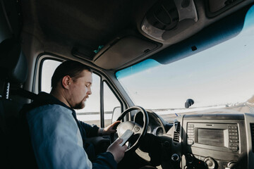 male truck driver is driving a truck on a sunny day with a smartphone.