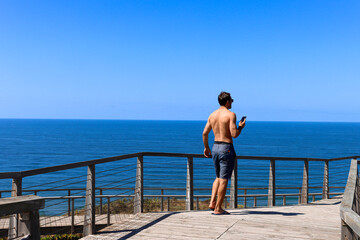 Young man traveler with his phone in his hands speaking in his headphones in a peaceful place in...