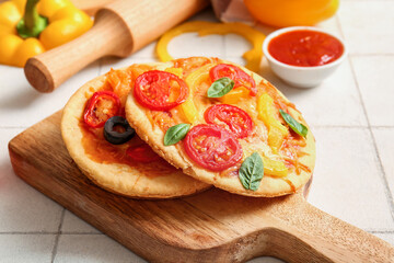 Board with different tasty mini pizzas on white tile background