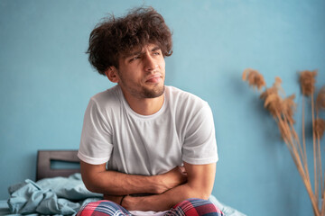 Young Arab man suffering for stomach ache sitting on bed at bedroom