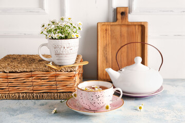 Composition with teapot, cup of natural chamomile tea and flowers on blue grunge table near wall