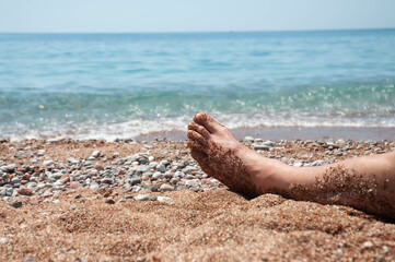 Leg of man in the sand on the beach next to the sea.