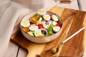 Tasty salad with quail eggs, tomatoes, onion and lettuce on light wooden background, closeup