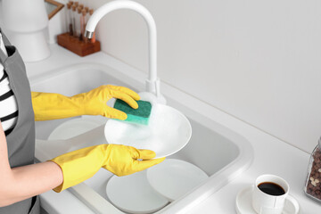 Woman in yellow rubber gloves washing plate with sponge in light kitchen - obrazy, fototapety, plakaty