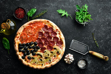 Homemade pizza with sausages, mushrooms, olives and tomatoes. Takeaway food. Home delivery of food. On a black stone background.