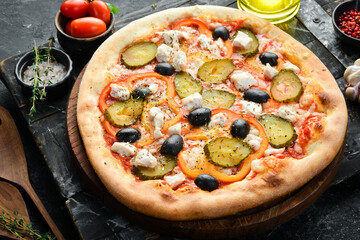 Homemade pizza: pickled cucumber, cheese and vegetables. Takeaway food. Home delivery of food. On a black stone background.