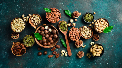 Peanuts, walnuts, almonds, hazelnuts and cashews mixed together in wooden bowls. Top view. On a dark background.