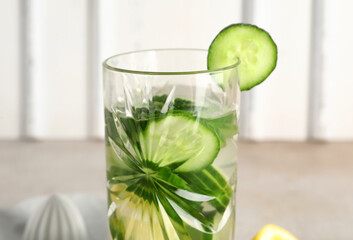Mason jar of infused water with cucumber slices and juicer on grey table