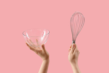 Female hands holding whisk and glass bowl on pink background