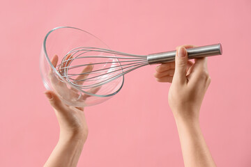 Female hands holding whisk and glass bowl on pink background
