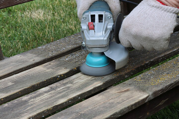 Removing lichens from a wooden surface of a garden bench with a metal brush and an angle grinder to...