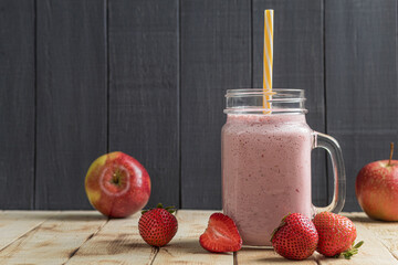 A glass of fresh strawberry milkshake, puree and fresh strawberries on a wooden background