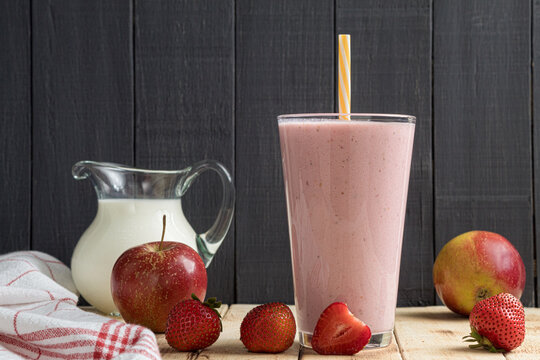 A glass of fresh strawberry milkshake, puree and fresh strawberries on a wooden background
