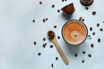 Cup of delicious coffee, wooden spoon, beans and capsules on blue table
