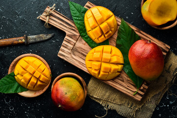 Ripe mango fruits cut on a wooden board. Tropical Fruits. On a stone background. Top view. Copy space.