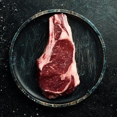 dry aged steak on the bone with spices and rosemary. On a black stone table. Top view.
