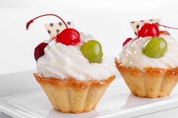 Beautiful cream cakes with cherries and grapes on a plate on a white background