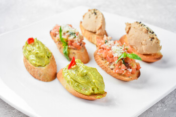 Set bruschetta. Sandwiches with avocado, liver pâté and vegetables. On a white plate. On a gray stone background. Restaurant menu.