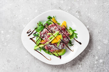 Salad: veal carpaccio, avocado, lettuce and orange. On a white plate. On a gray stone background. Restaurant menu.