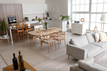 Interior of light open plan kitchen with dining table, island and grey sofa