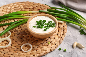 Bowl of tasty sour cream with sliced scallion and onion on grey background