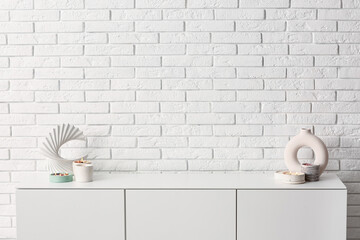 Chest of drawers with burning candles and decor near light brick wall in room