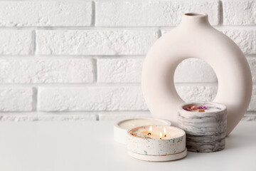 Holders with burning candles and decor on table near light brick wall in room