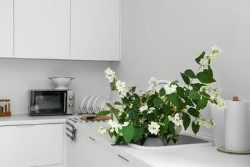 Vase with blooming jasmine flowers in kitchen sink
