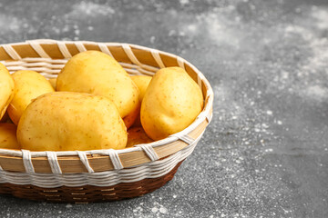 Wicker bowl with raw baby potatoes on grey background