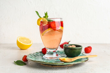 Glass of infused water with strawberry and lemon on light background