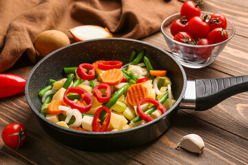 Frying pan with fresh vegetables on wooden background