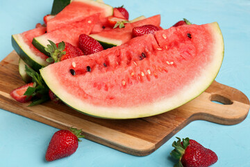 Board with pieces of fresh watermelon and strawberries on blue background