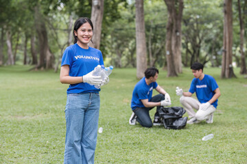 A group of happy young Asian volunteers in uniform stand in a public park with plastic garbage bags, helping their community by cleaning up an area in the park.