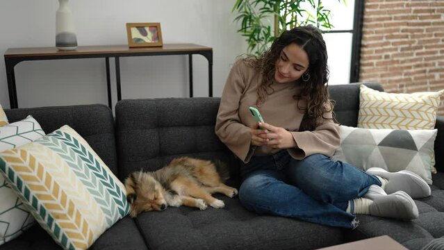 Young hispanic woman with dog make photo by smartphone to asleep dog at home