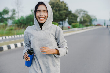 asian muslim woman running and exercising while holding drink bottle outdoors excitedly