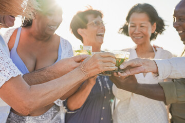 Senior friends cheering with mojito on the beach during travel vacation - Elderly multiracial people having fun together - Focus on the hands