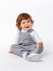 A cheerful, mischievous 2-year-old toddler with curly hair in a gray jumpsuit and a white...
