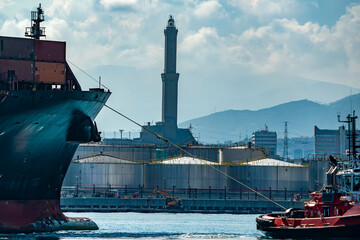 A tug tows a container ship in the port of Genoa, Italy near The Lanterna a lightouse Symbol of the...