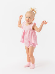 Indignation, surprise. A 1-2-year-old toddler girl in a cute pink dress in socks stands with her hands raised on a white background.